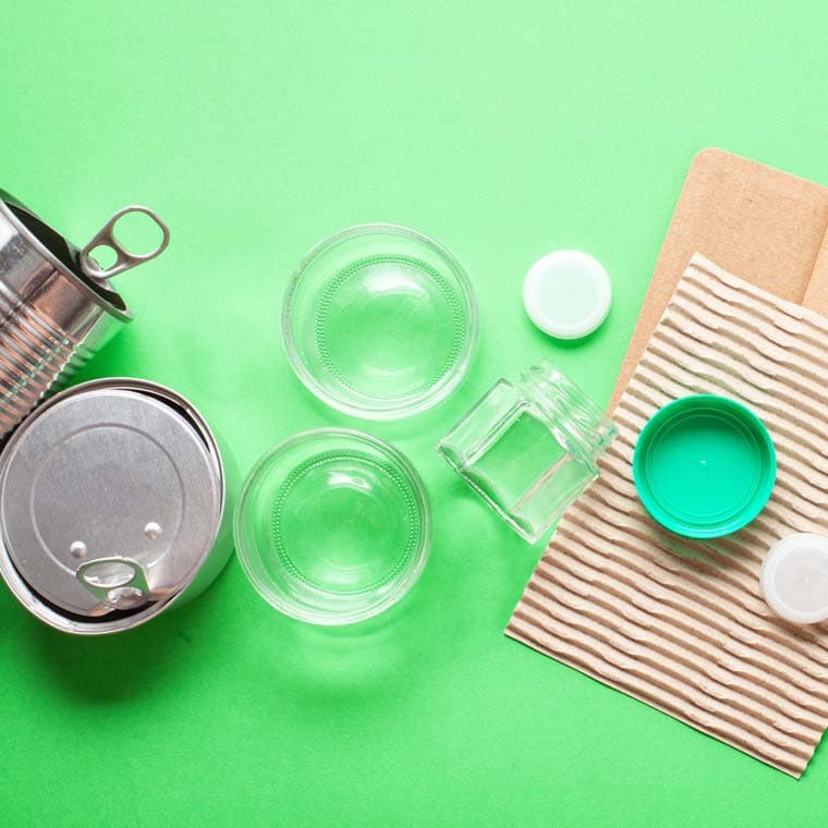 Tomma förpackningar av olika materialslag mot en grön bakgrund.