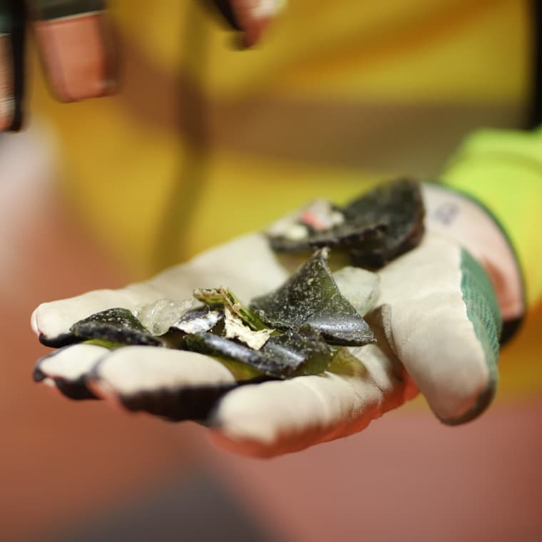 Närbild på en hand med en arbetshandske som håller i färgade glasskärvor.