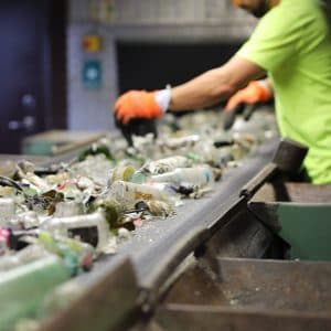 En person sorterar glasförpackningar vid ett löpande band