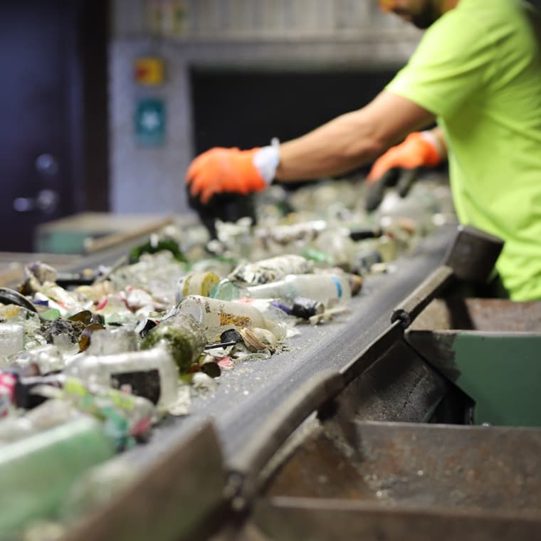 En person sorterar glasförpackningar vid ett löpande band