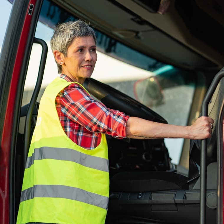 Kvinna med reflexväst kliver in i förarhytten på en arbetsbil.