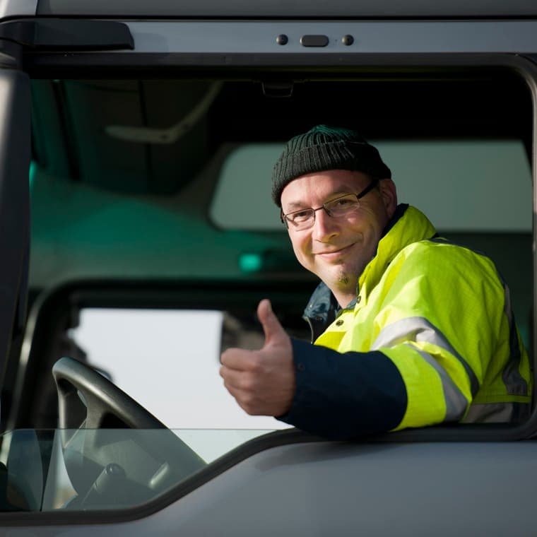 Lastbilschaufför som sitter i förarhytten och gör tummen upp.