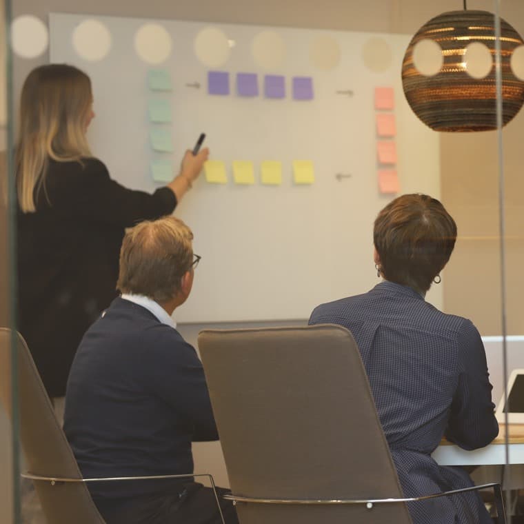 Tre personer som tittar på en whiteboard-tavla i ett konferensrum.
