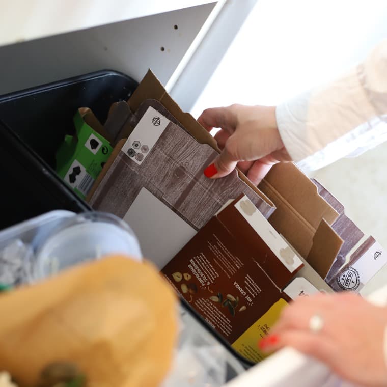 Hand som källsorterar en pappersförpackning i pappersbehållaren i ett kök.