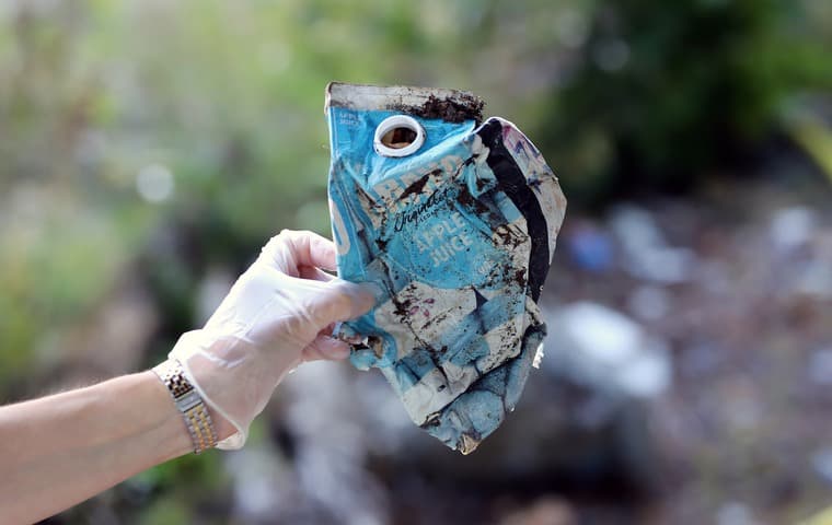 En hand håller upp en förpackning som skräpat ned.