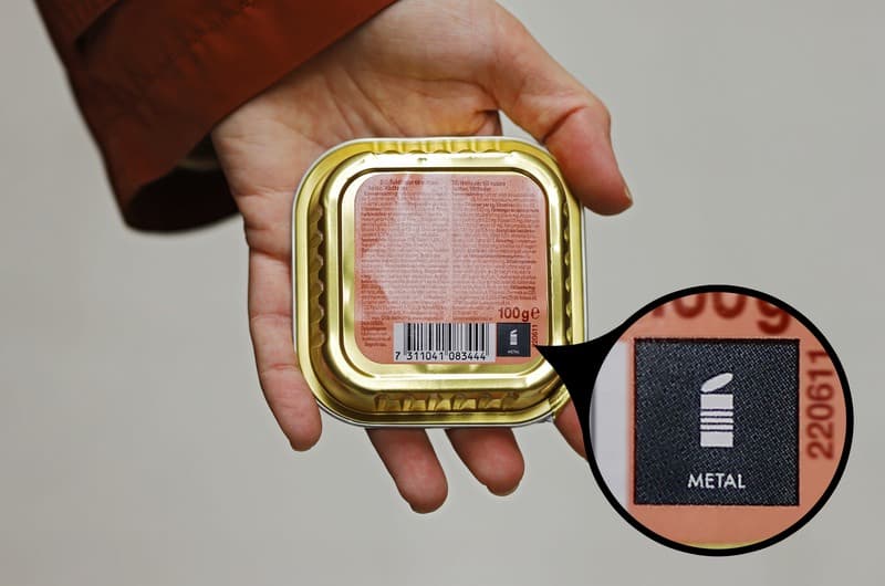 En hand som håller upp en förpackning med kattmat med märkning som visar att förpackningen ska källsorteras som metall.