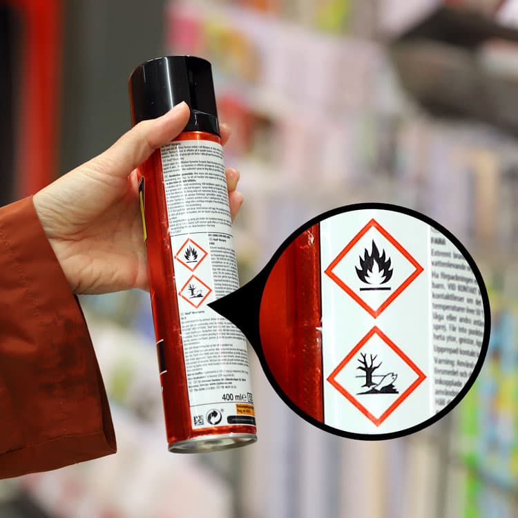 En hand som håller upp en sprayflaska med märkning som visar att förpackningen ska sorteras som farligt avfall.