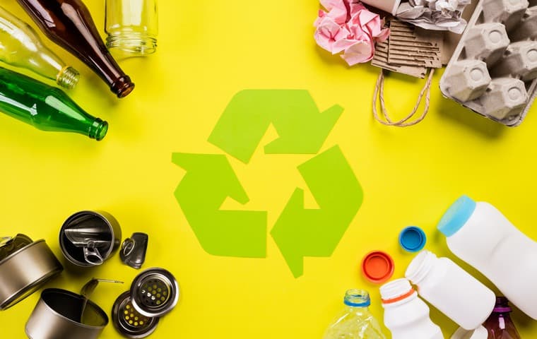 Förpackningar av olika materialslag ligger i olika hörn mot en gul bakgrund. I mitten finns en grön återvinningssymbol.